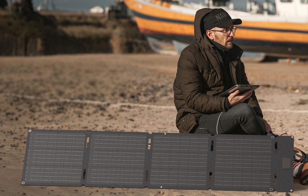 ężczyzna siedzący na plaży z tabletem obok rozłożonego panelu solarnego EcoFlow